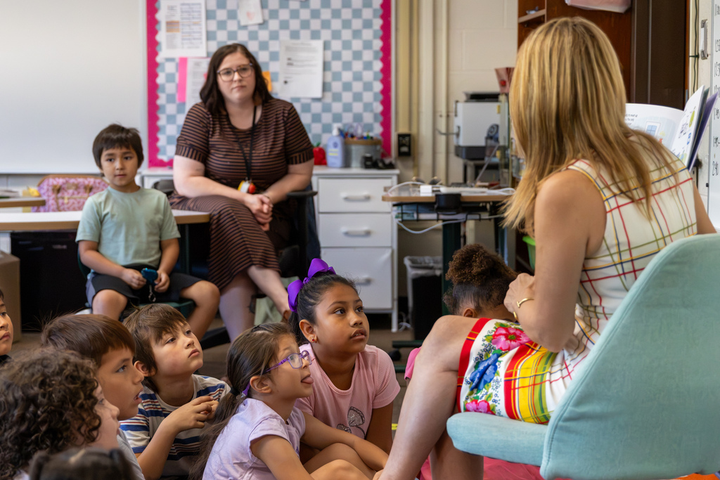 Representative Hefner makes an animated expression while holding an open picture book beside her in front of a classroom whiteboard.