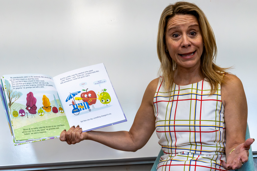 Representative Hefner makes an animated expression while holding an open picture book beside her in front of a classroom whiteboard.