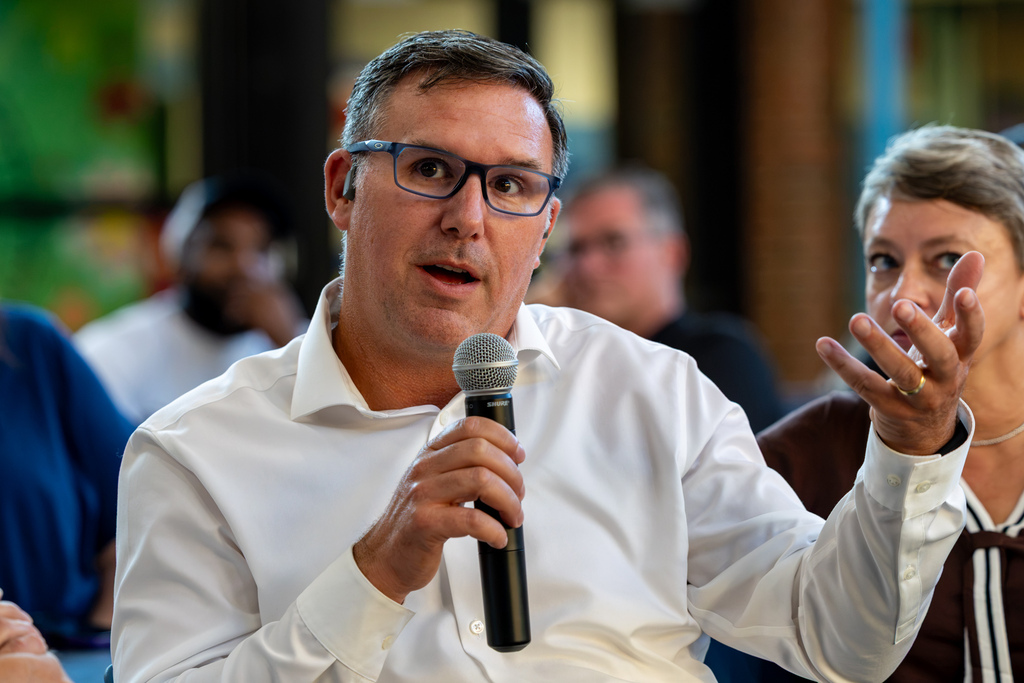 A man wearing glasses speaks into a microphone and gestures with one hand while participating in the Real Talk conversation.