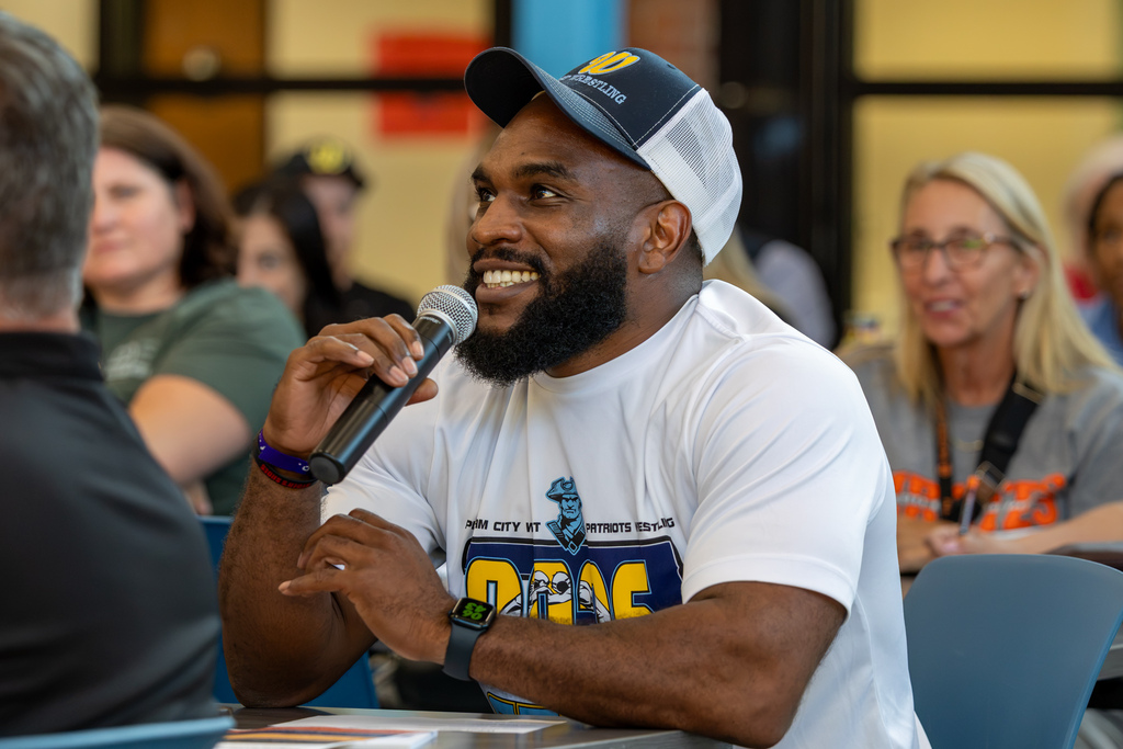 A smiling PC West attendee wearing a wrestling shirt and cap speaks into a handheld microphone during the community conversation.