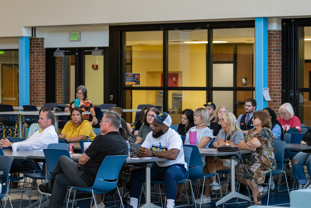 Community members sit around tables listening attentively during the Real Talk with district leadership event at PC West.