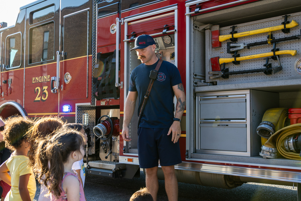 A Warr Acres firefighter shows Smart Start students the axes and other tools stored in an open compartment on Engine 23.