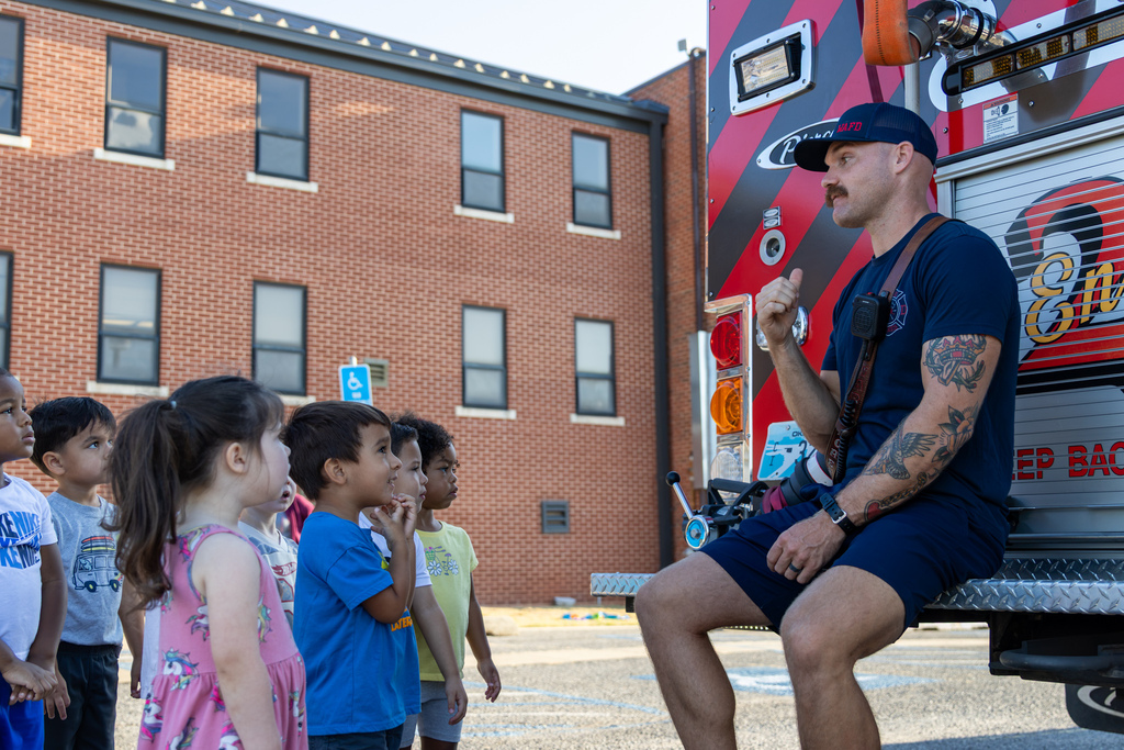 Smart Start students listen closely as a Warr Acres firefighter speaks to them while seated on the back of Engine 23.