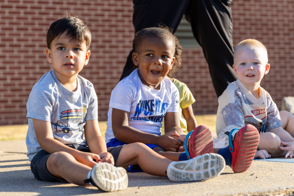 Three Smart Start students sit together outside and watch the fire-truck demonstration.