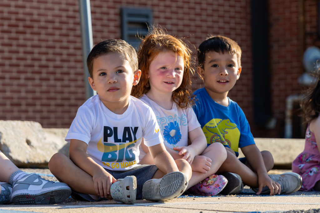 Three Smart Start students sit side by side while watching firefighters demonstrate their equipment.