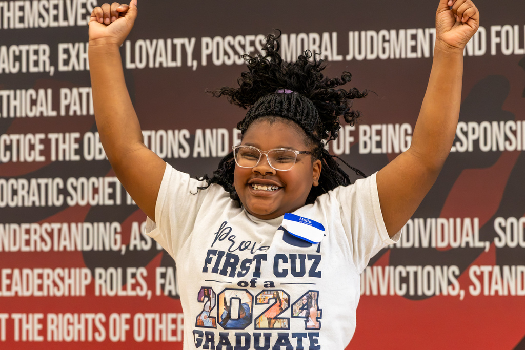 A smiling young dancer with glasses raises both arms overhead during practice, her hair moving as she performs the routine.