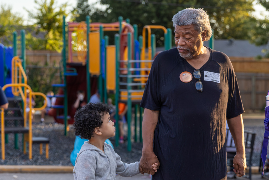 A young student holds hands with an older family member as they walk beside the playground.