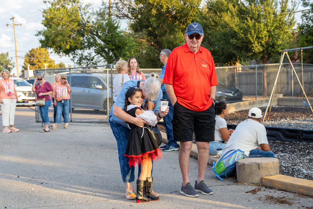 An older woman hugs a young girl near the playground while another family member stands beside them.