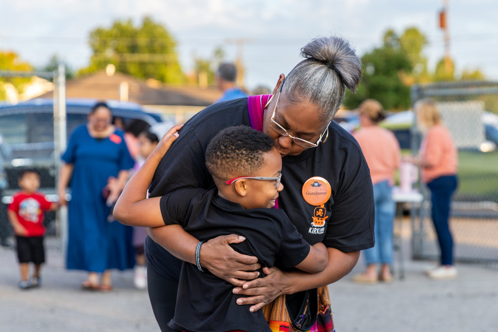 An older woman bends down to hug a smiling student during Goodies with Grands outside DD Kirkland.