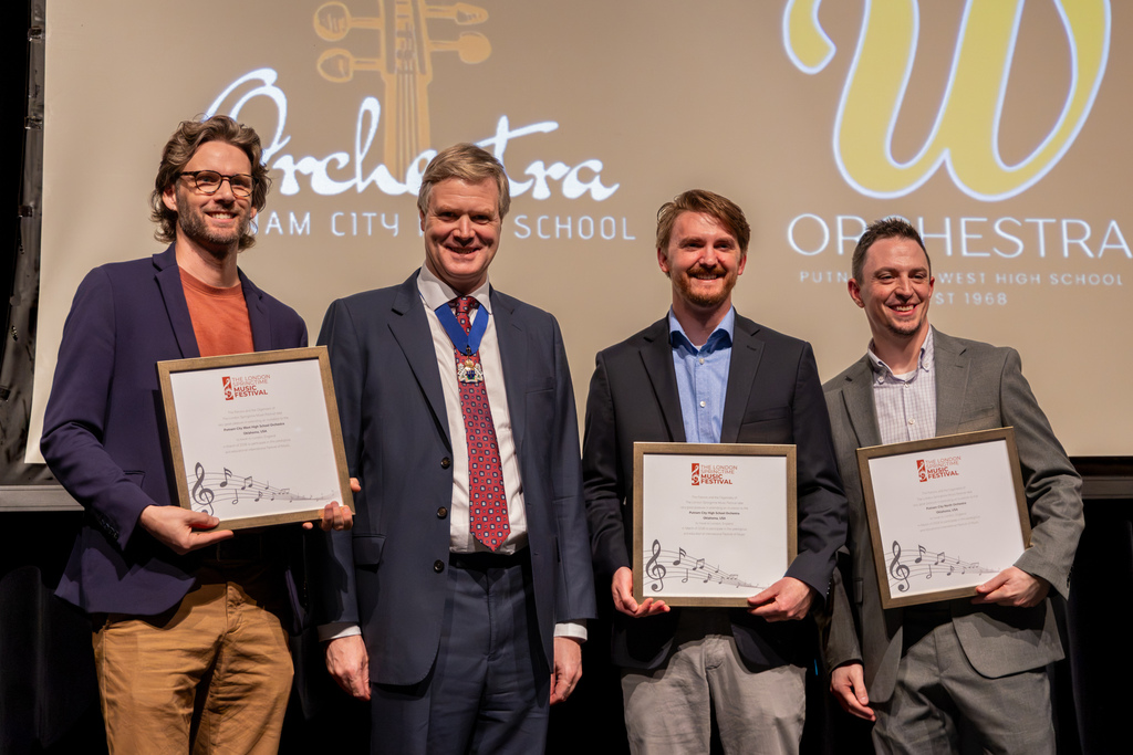 The three Putnam City high school orchestra directors pose with a London Springtime Music Festival representative, holding framed invitations following the announcement.