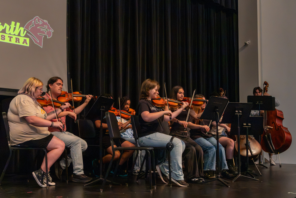 Putnam City orchestra students perform on stage, with violin, viola, cello, and double bass players seated behind music stands.