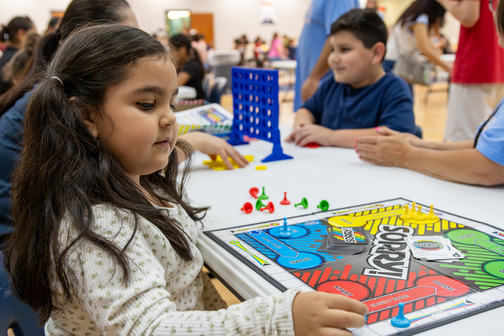 A young girl concentrates on a game of Sorry! while other students and family members play games at tables around her during Central Elementary’s Family Game Night.