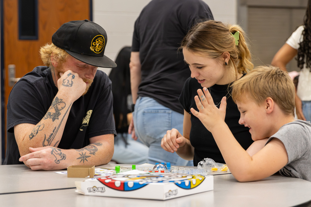 A student laughs and raises his hand while playing Trouble with two adults during Central Elementary’s Family Game Night.