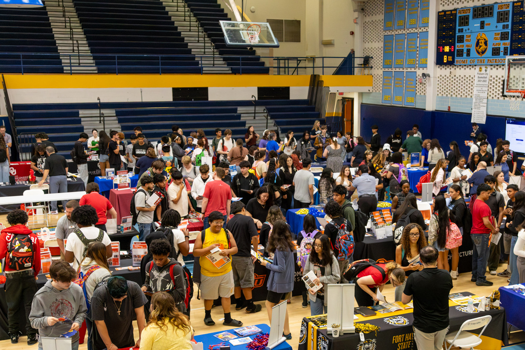 Wide view of the PC West gym filled with students visiting college and university booths during the Putnam City college fair.