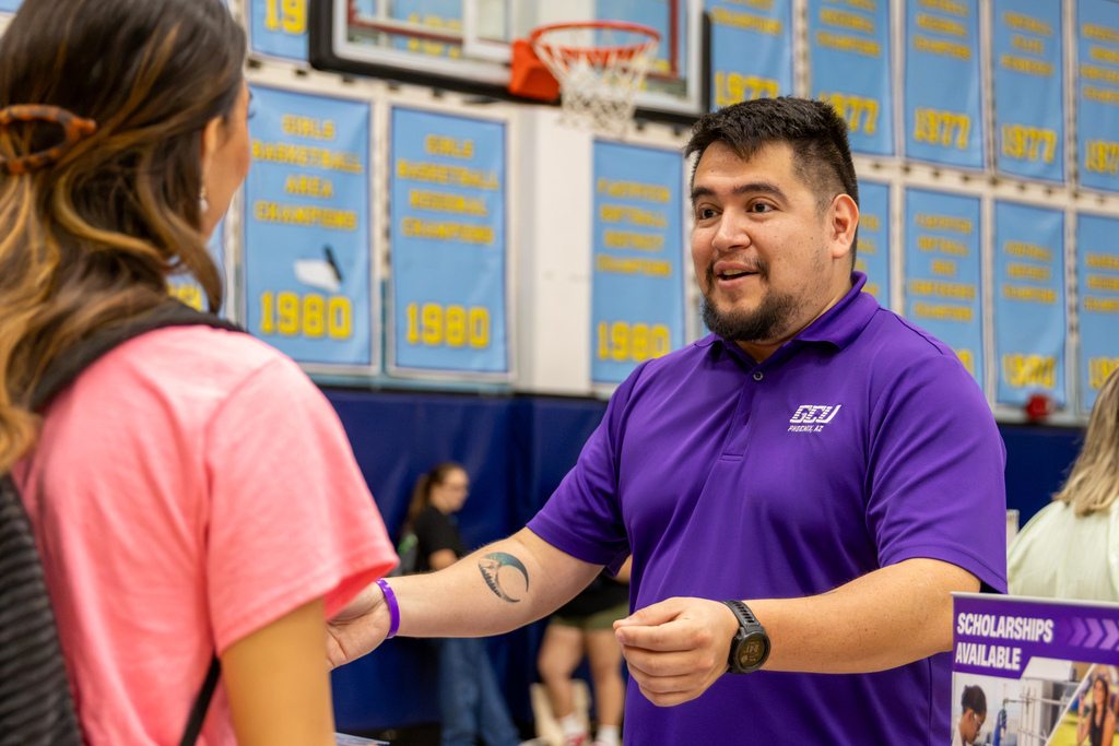 A Grand Canyon University representative speaks with a student at a college fair table.