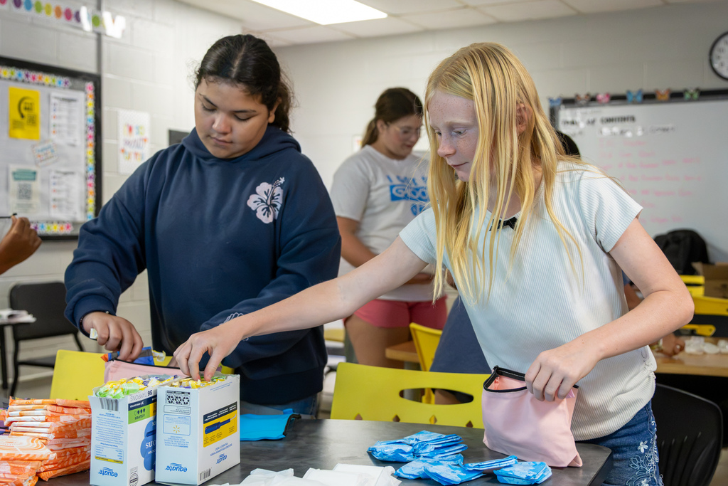 Two Western Oaks Middle School softball players fill colorful zippered hygiene bags with donated personal care items in a classroom.