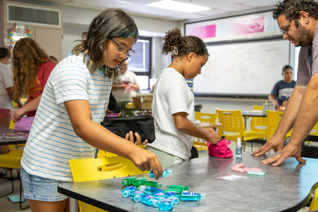 A Western Oaks Middle School student places a small bottle of personal care product into a hygiene bag while teammates work around the classroom.
