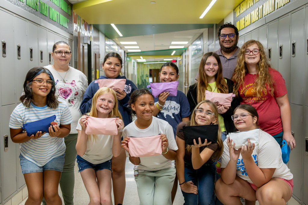 Western Oaks Middle School softball players and their coaches pose in a school hallway holding the completed hygiene bags they assembled for City Center.
