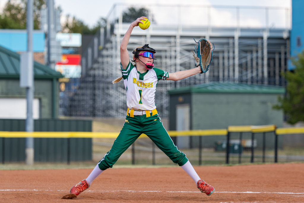 A Western Oaks pitcher begins her windup, raising the softball overhead before delivering the pitch.