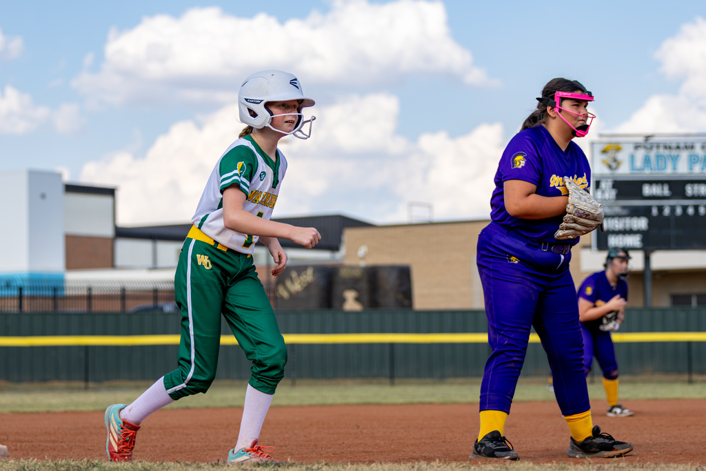 A Western Oaks player in green and white leads off a base while a Mayfield infielder in purple watches the play.