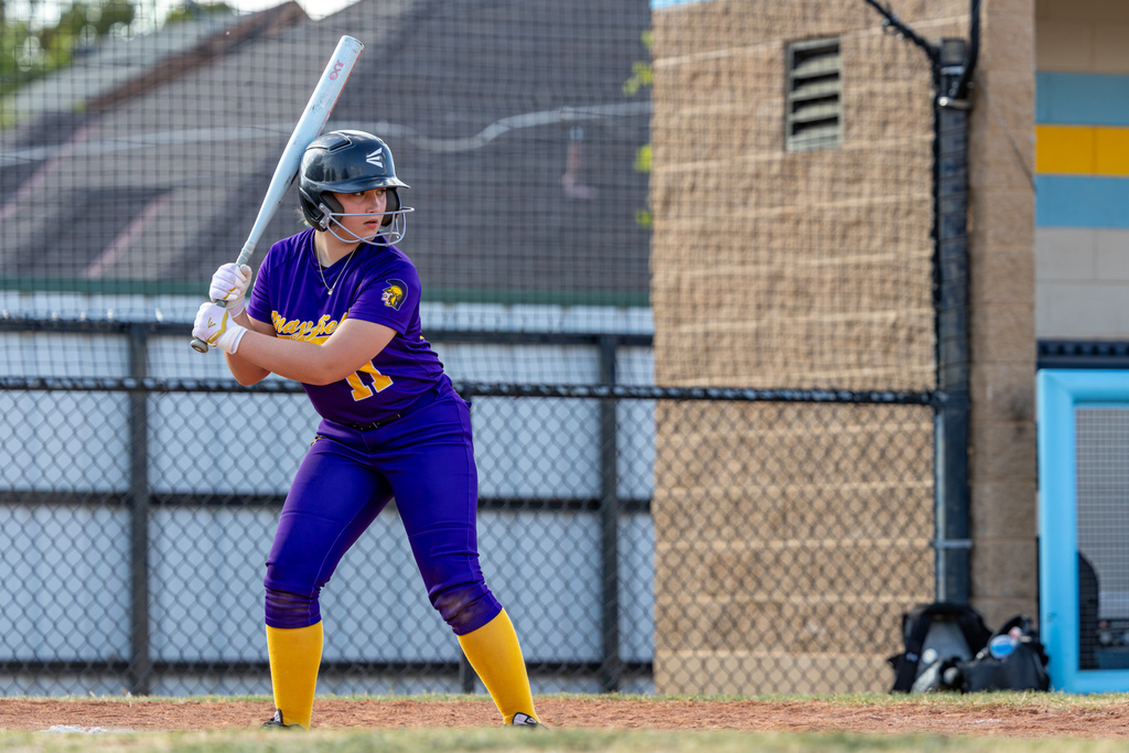 A Mayfield batter in a purple uniform waits at the plate with her bat raised.