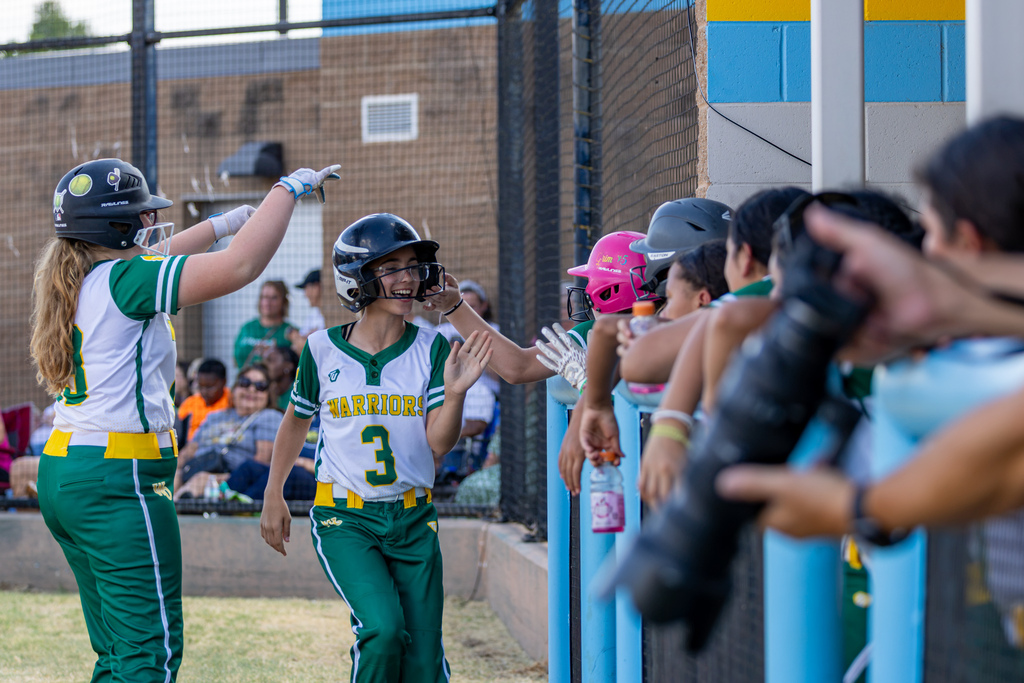 A smiling Western Oaks player returns to the dugout and high-fives teammates along the fence.
