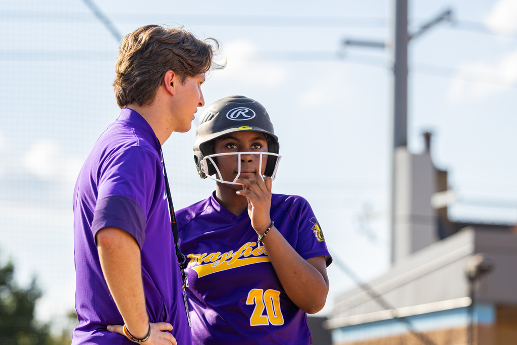 A Mayfield coach speaks with a player wearing a batting helmet during a break in play.