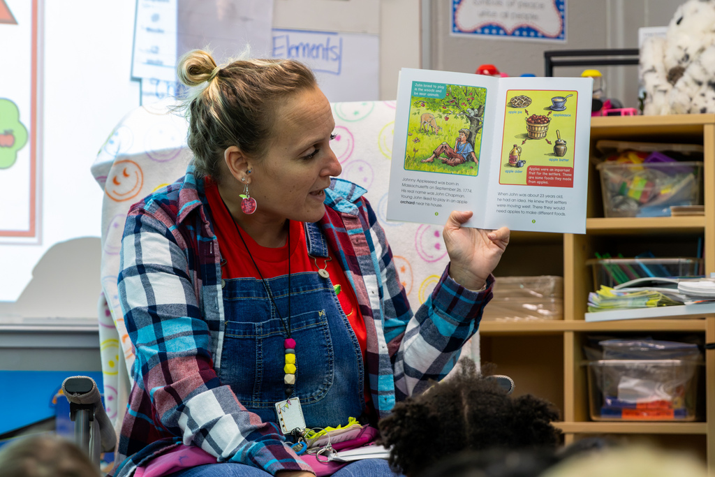 Mrs. Ingram holds up an illustrated book about Johnny Appleseed while reading to her kindergarten class.