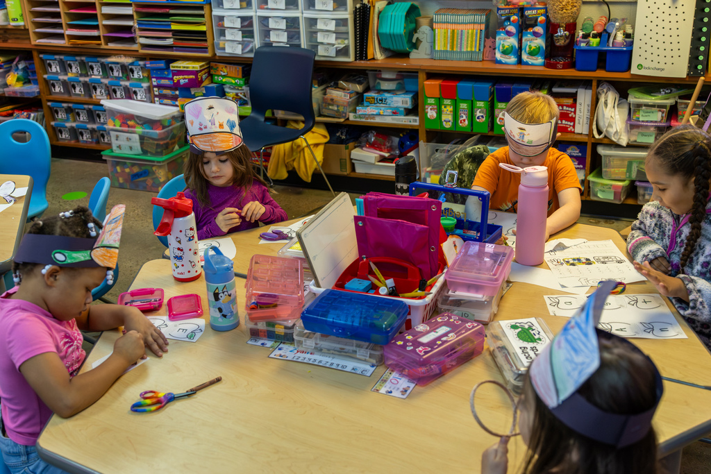 Kindergarten students sit around a classroom table cutting, coloring, and assembling their Johnny Appleseed pan hats.