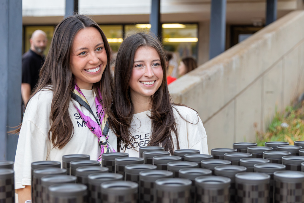 Two Simple Modern representatives smile behind a display of black checkered tumblers prepared for distribution to families.