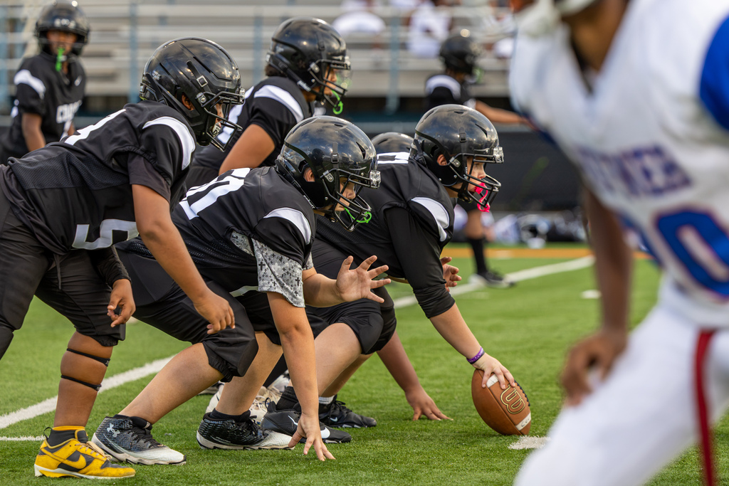 Cooper Middle School football players in black line up at the line of scrimmage as the center reaches down to the football before the snap.