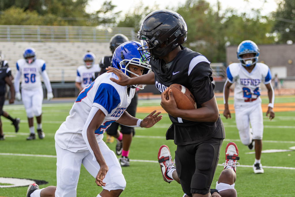 A Cooper Middle School ball carrier in black protects the football while a Hefner defender in white and blue closes in for a tackle.