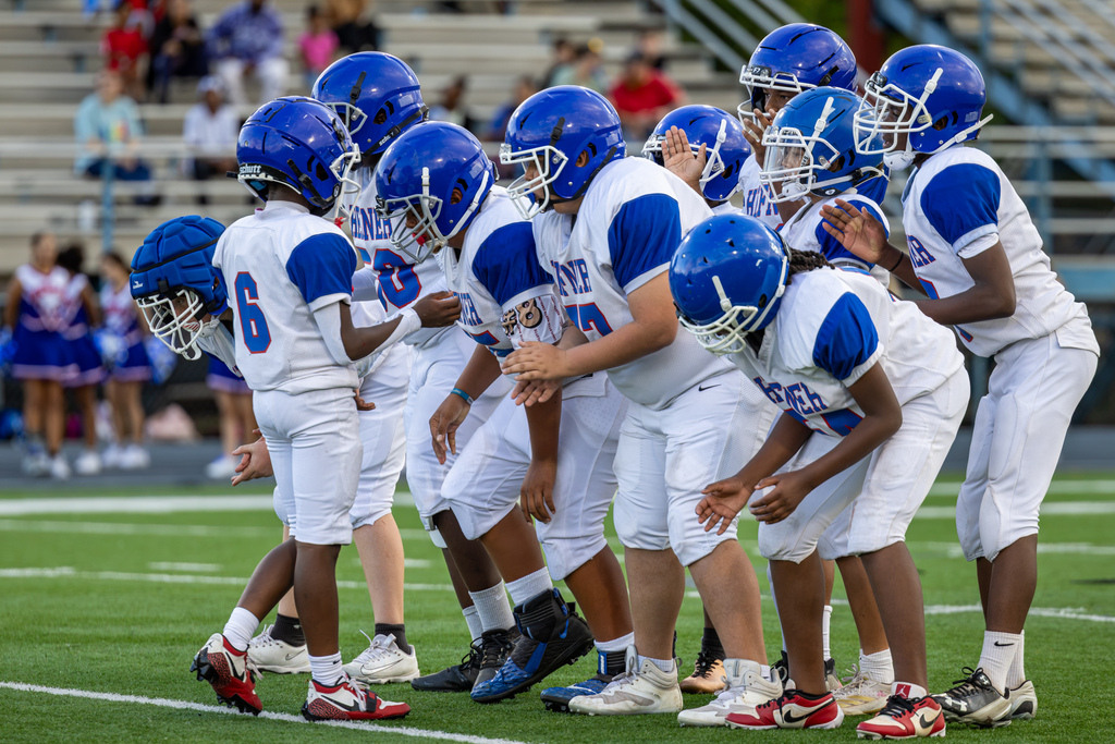 A group of Hefner Middle School football players in white and blue uniforms huddle together on the field before the next play.