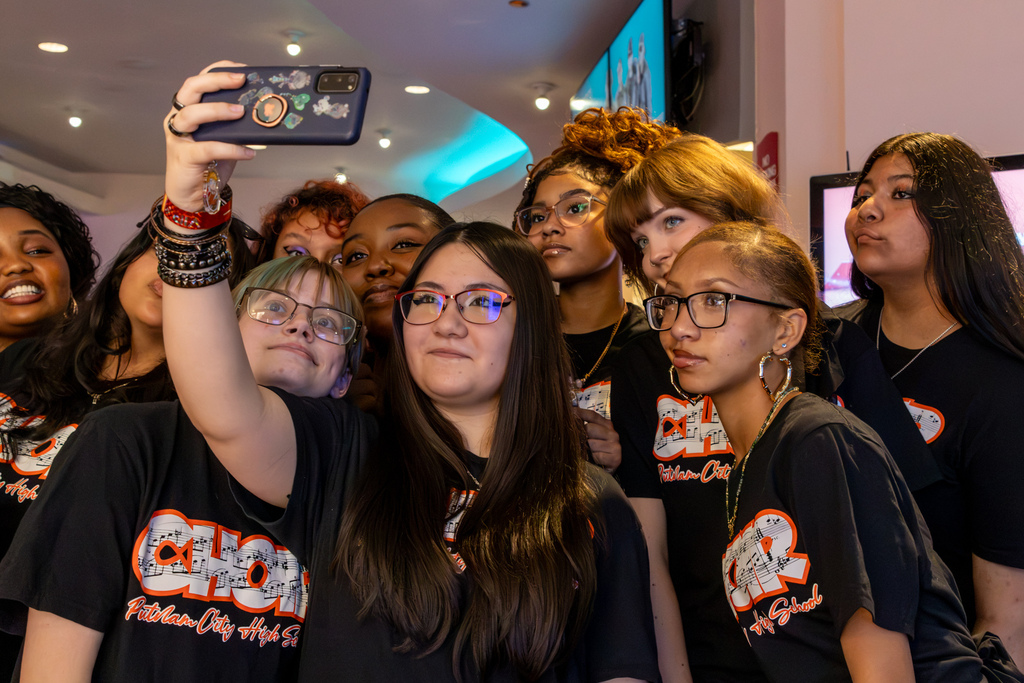 Putnam City High School choir students crowd together and smile while one student holds up a phone to take a group selfie.
