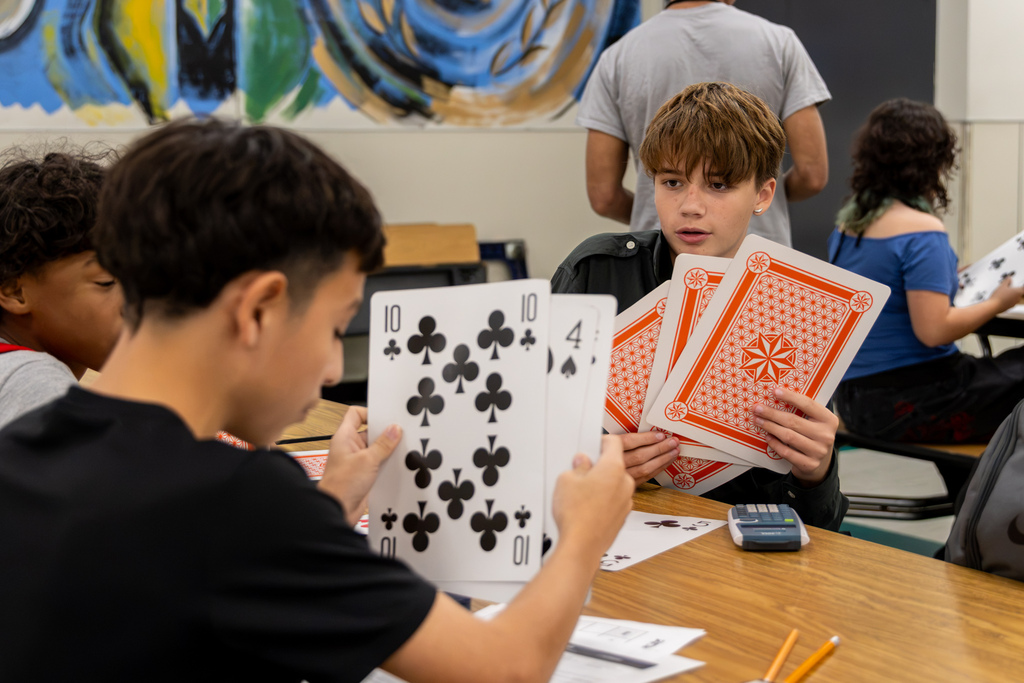 Western Oaks Middle School students use oversized playing cards during a math activity at a table.