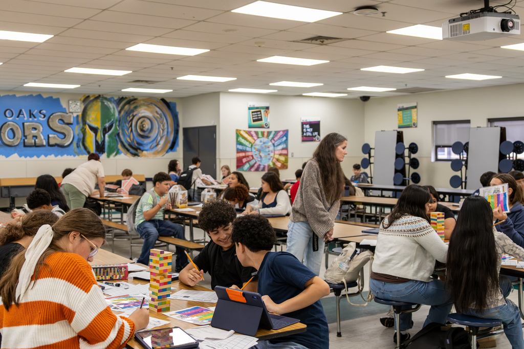 Western Oaks Middle School students work in small groups around the classroom using cards, dice, worksheets, and block towers for math activities.