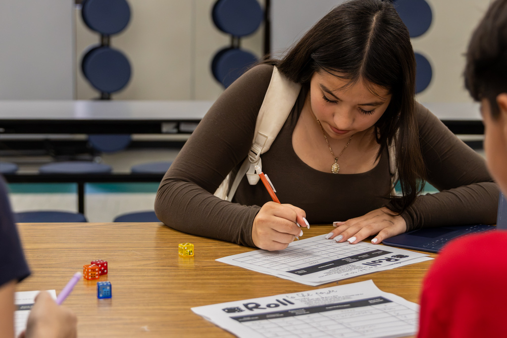 A Western Oaks Middle School student writes on a math worksheet beside several colorful dice during an exponent activity.