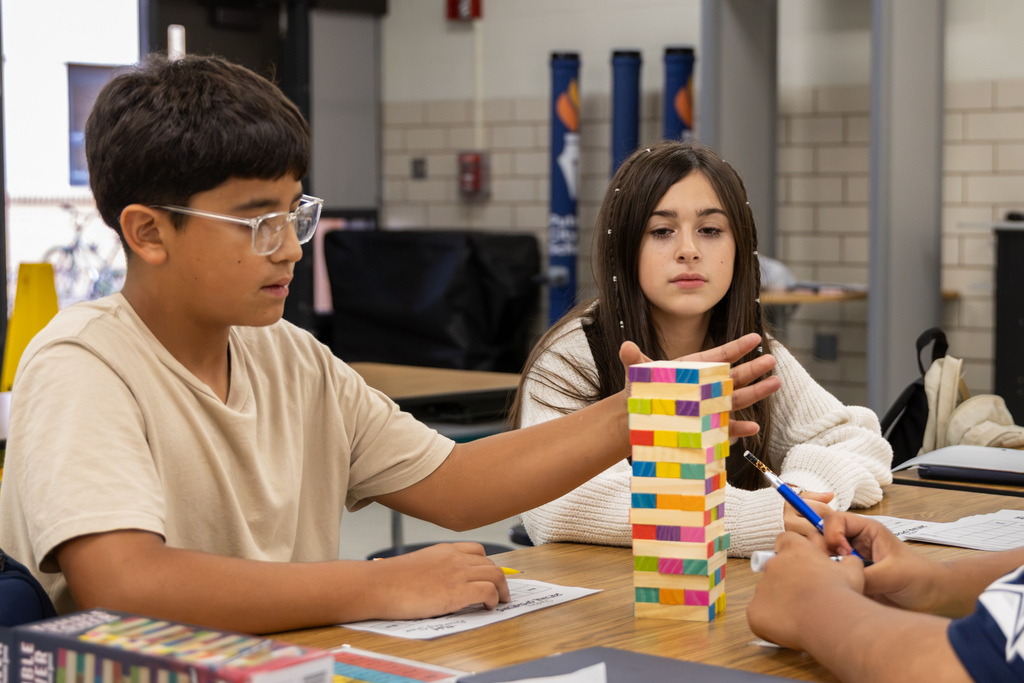 Two Western Oaks Middle School students play a math game using a colorful wooden block tower while classmates work nearby.