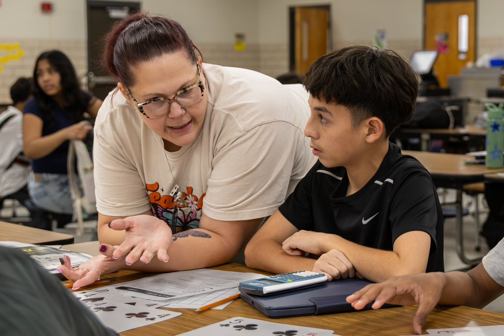 A Western Oaks Middle School teacher helps a student work through a math activity using cards, a calculator, and a worksheet.