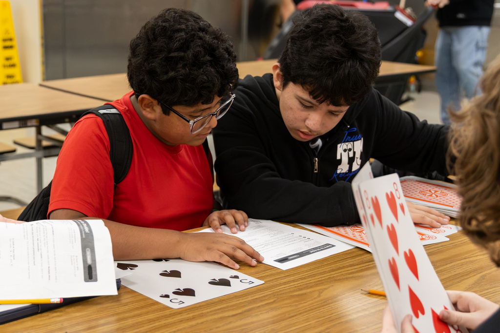 Two Western Oaks Middle School students work together on a math worksheet while oversized playing cards are spread across the table.