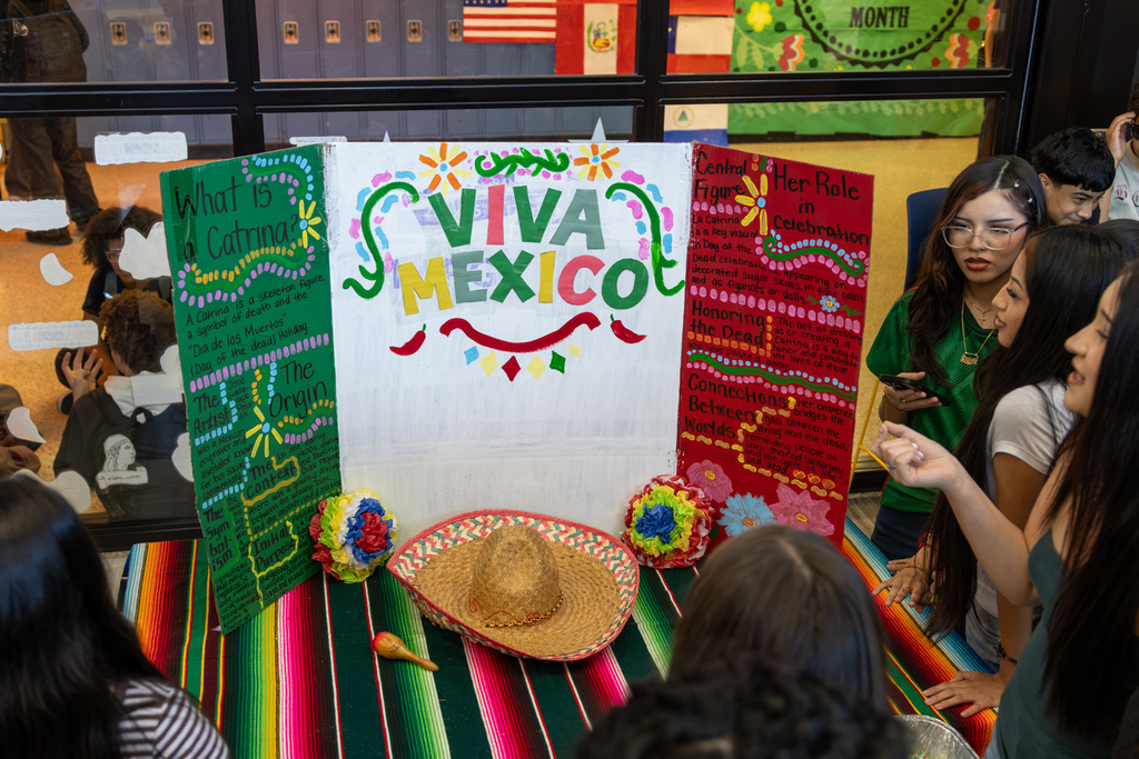 Students gather around a colorful “Viva Mexico” display explaining La Catrina and Día de los Muertos traditions.