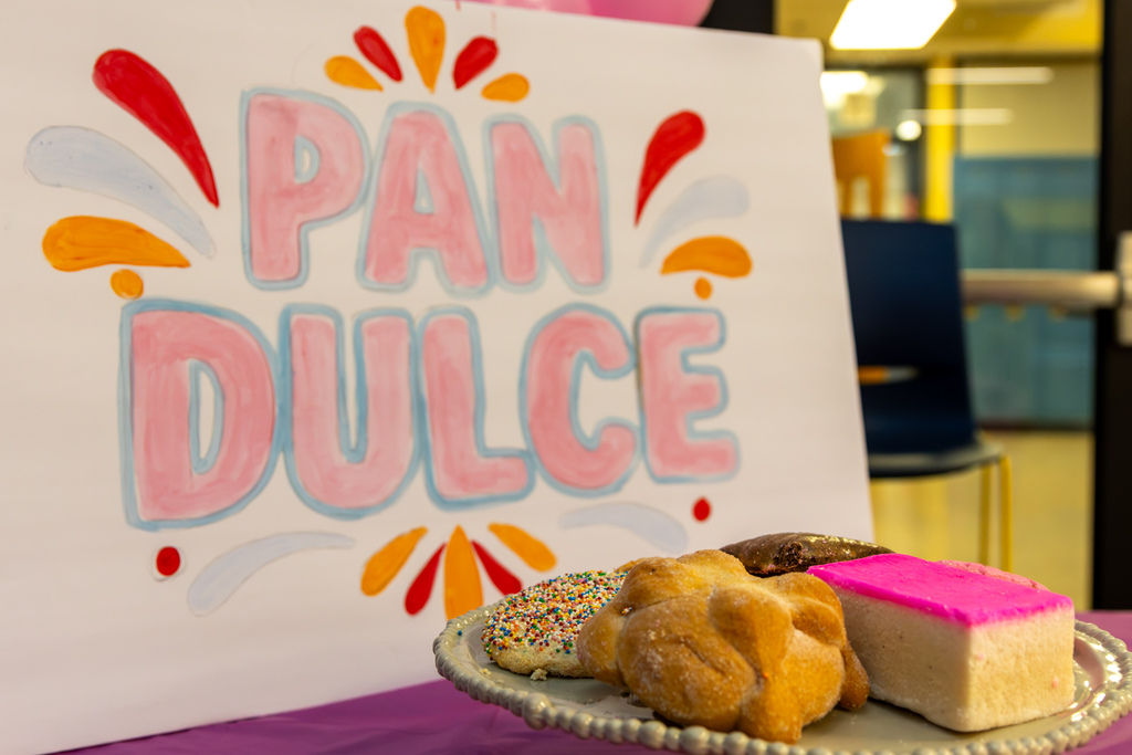 A display of pan dulce and other sweet breads sits in front of a hand-drawn “Pan Dulce” sign.