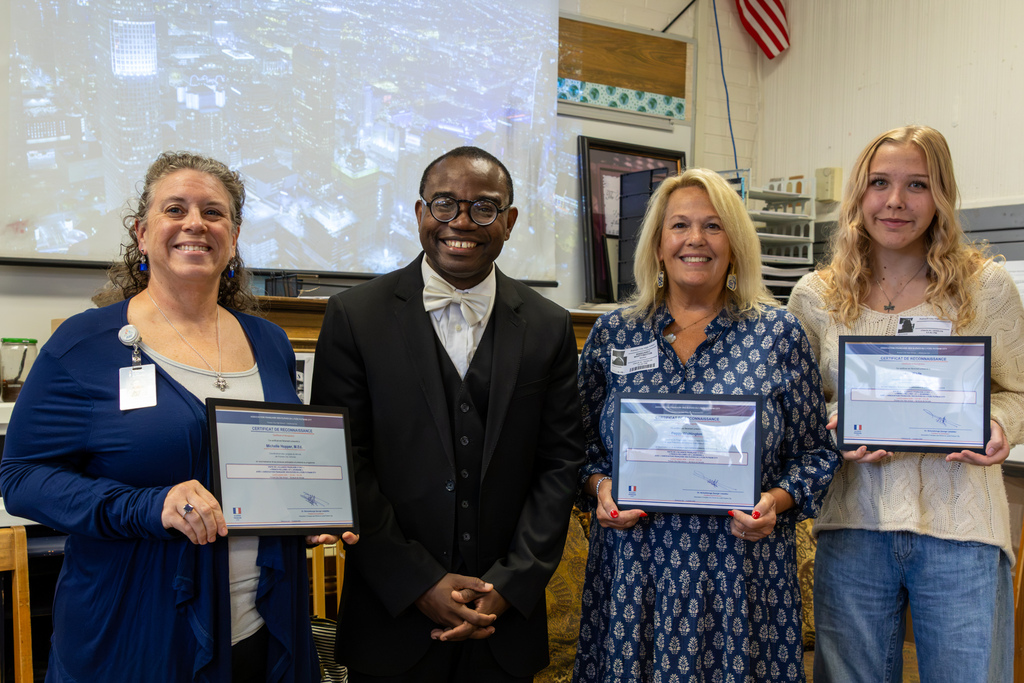 Putnam City staff, Alliance Française representatives, and a former program participant pose together holding certificates after the presentation.