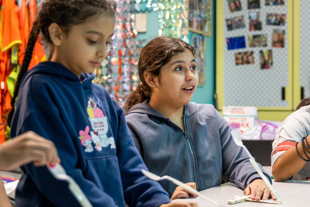 Two Western Oaks Elementary students work on their catapults, with one looking up excitedly while the other examines her project.