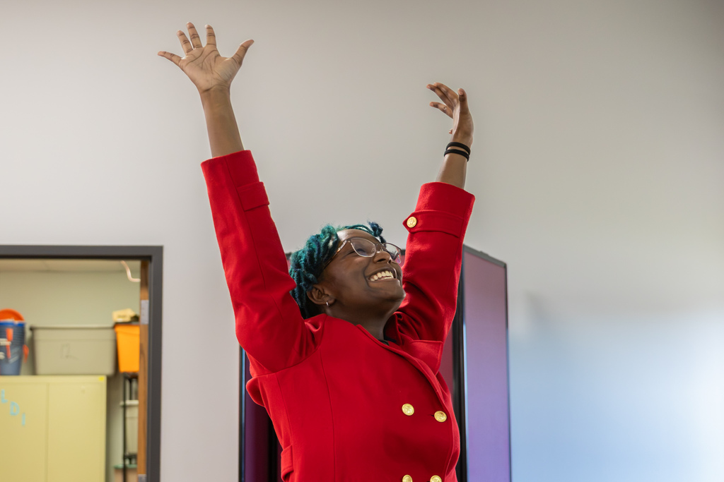 A Putnam City North student wearing a bright red blazer throws both arms into the air with a wide smile, celebrating after the Mongol Empire is found guilty during an AP World History mock trial.