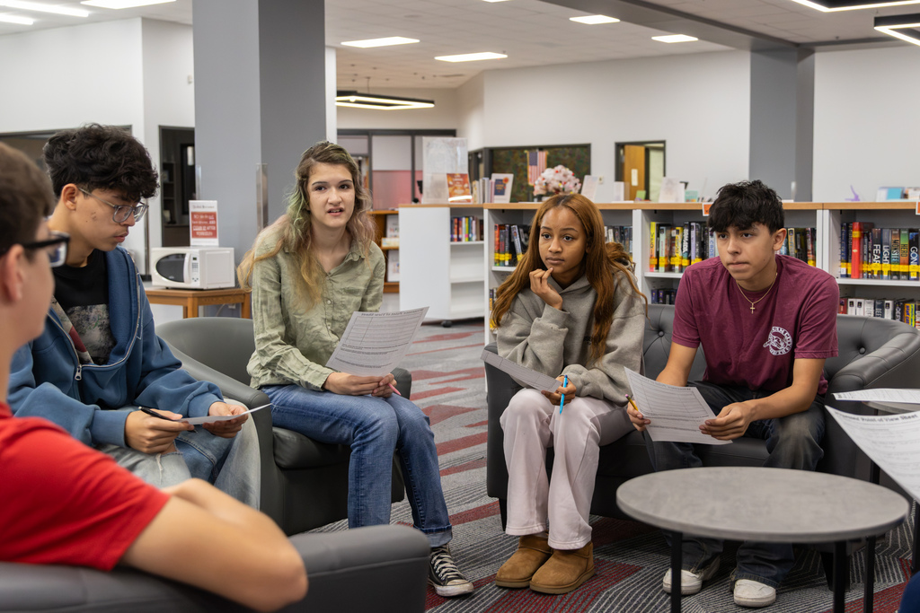 Five Putnam City North students sit in a circle in the library, holding worksheets and discussing evidence during an AP World History mock trial.