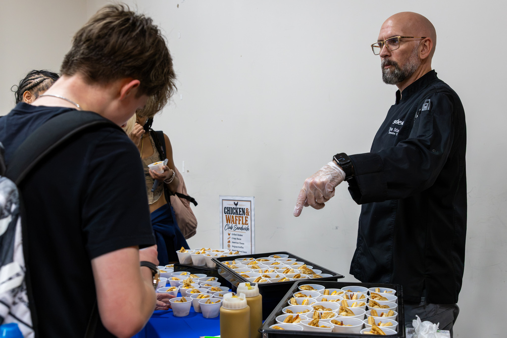 Sodexo Executive Chef Tyler Stinson gestures toward trays of chicken and waffle sandwich samples while speaking with Putnam City High students during a lunch taste test.