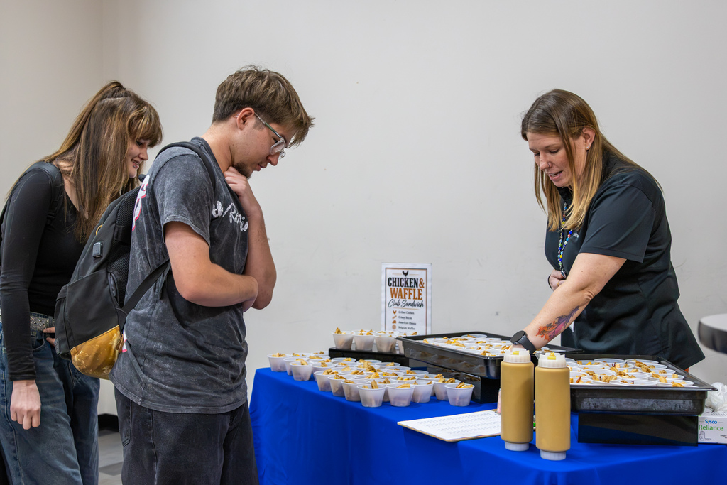 Two Putnam City High students examine chicken and waffle sandwich samples as a Sodexo employee explains the food options at a taste-testing station.