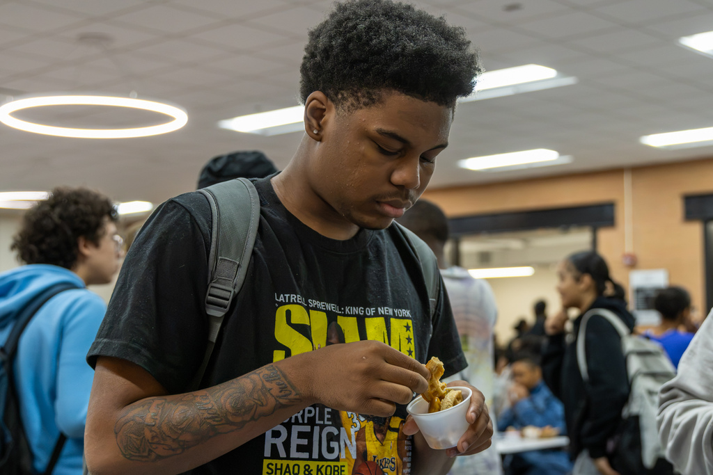 A Putnam City High student wearing a black graphic T-shirt holds a sample cup and examines a piece of the chicken and waffle club sandwich during Sodexo's taste test.