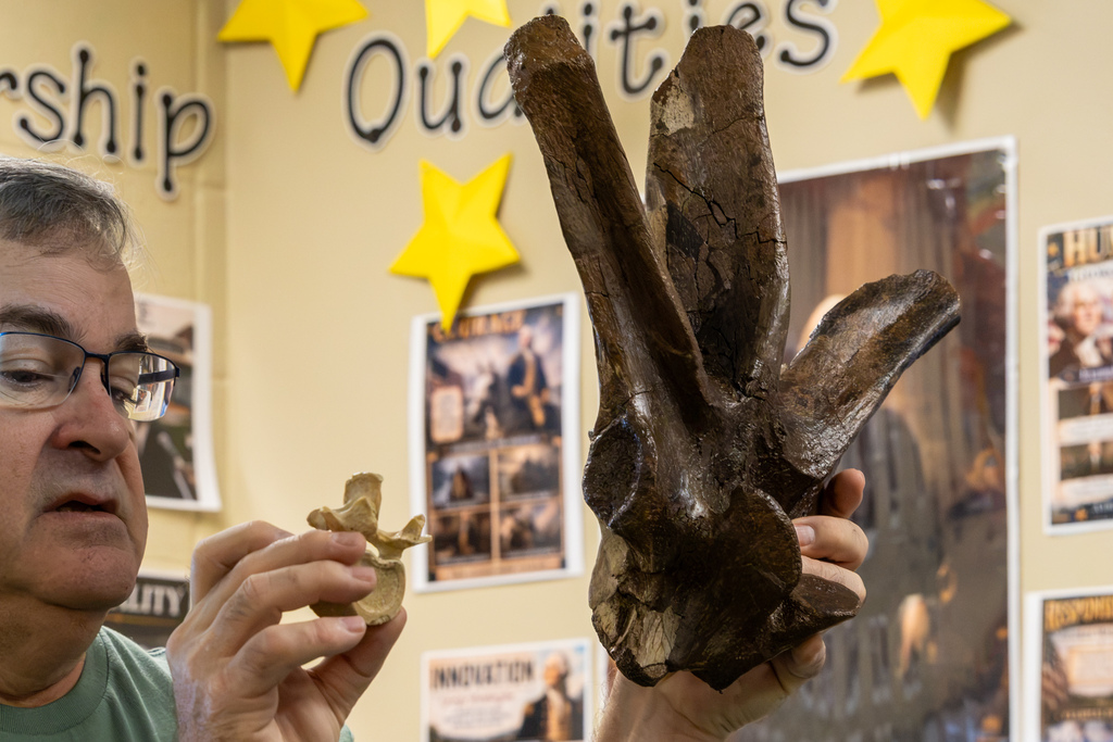 Dale Utt holds up a large, dark fossilized bone while comparing it with a smaller specimen during a classroom presentation.